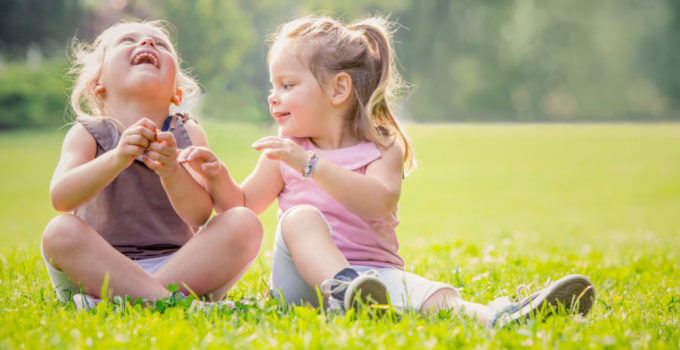 blonde smiling sister play in a garden